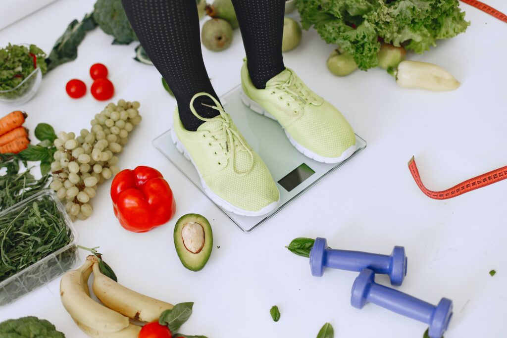 Person standing on a scale surrounded by healthy foods | The 'Beta Diet Plan': How Exercise and Weight Loss Play a Role in Your Metabolic Health